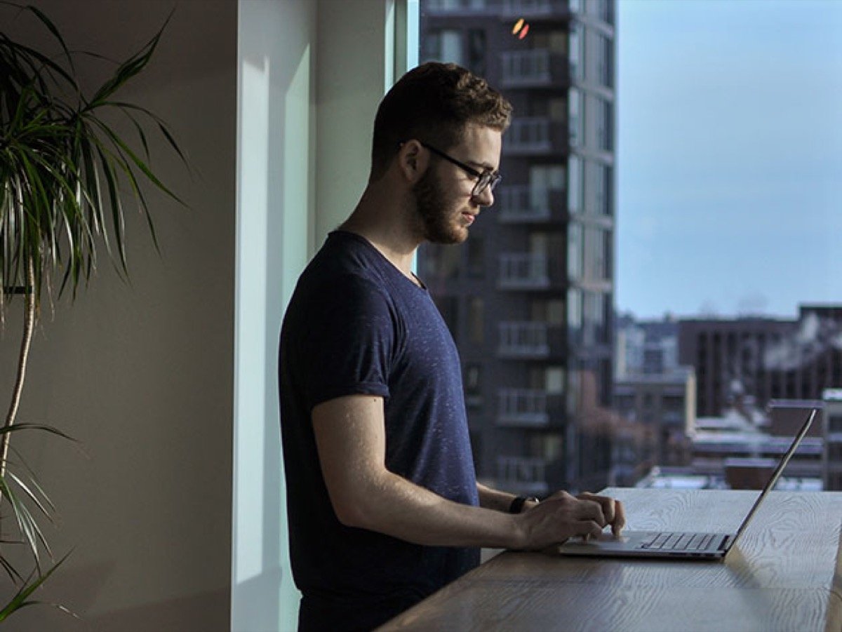 Man standing while using a laptop computer at his waist height like a goober.