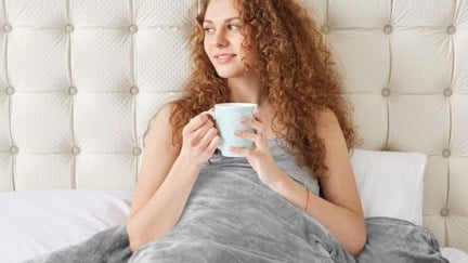 A woman drinking from a mug in bed, as you do.