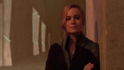 Carol Danvers leans against a wall and smirks.