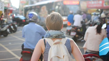 A woman wearing a backpack, walking through a crowded city.