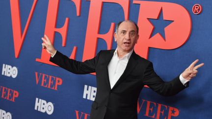 Armando Iannucci does the Nixon peace sign pose in front of the VEEP logo.