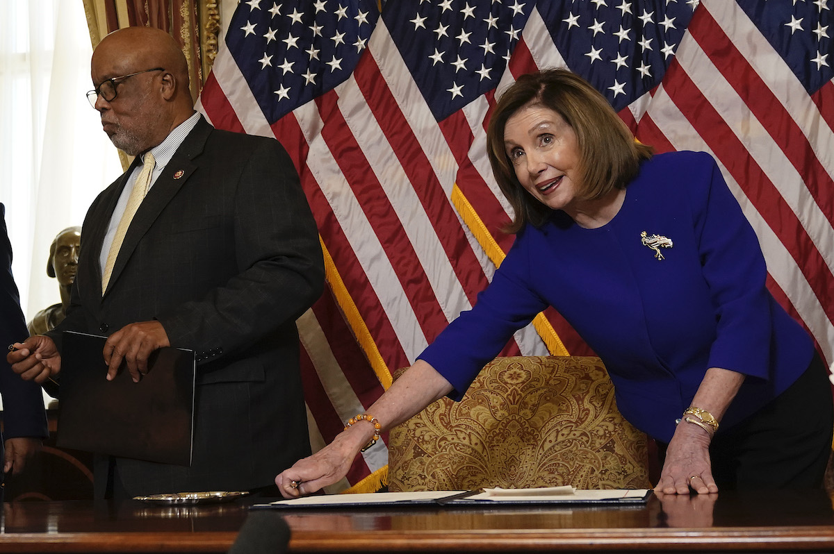 Nancy Pelosi leans over a desk in front of US flags.