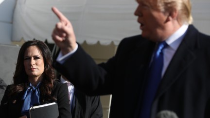 White House Press Secretary Stephanie Grisham (L) listens to U.S. President Donald Trump talk to reporters