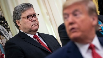 Attorney General William Barr frowns at Donald Trump, sitting in front of him, out of focus.