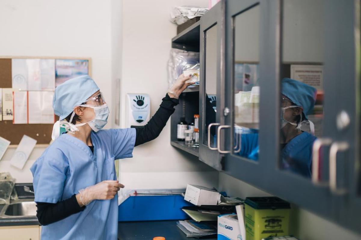 A doctor in surgical attire reaches up to a shelf.