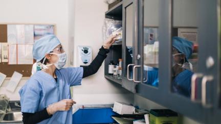 A doctor in surgical attire reaches up to a shelf.