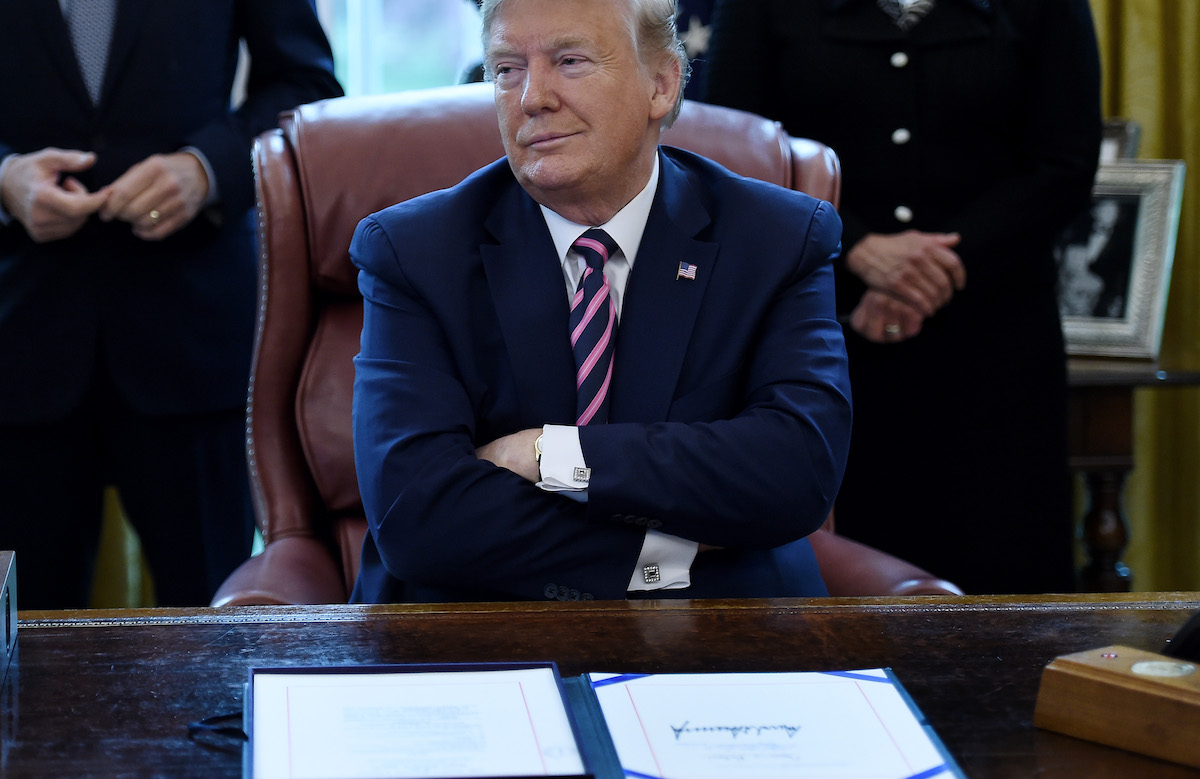 Donald Trump folds his arms and looks smug sitting behind the Oval Office desk.