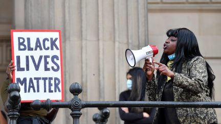 A protester addresses others through a megaphone as another holds a placard with the lettering reading 'Black lives matter' in Liverpool, northwest England, on June 2, 2020, during a demonstration after George Floyd, an unarmed black man, died after a police officer knelt on his neck during an arrest in Minneapolis, USA. - The city of Liverpool lit up their civic buildings in memory of George Floyd on June 2 the death of whom in Minneapolis while in police custody has sparked days of unrest in the US city and beyond. (Photo by Paul ELLIS / AFP) (Photo by PAUL ELLIS/AFP via Getty Images)