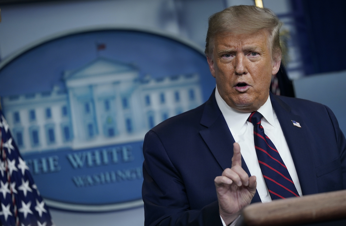 Donald Trump holds his index finger up at reporters during a press briefing.