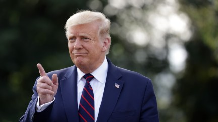 Donald Trump points upward while talking to the press outside of the White House.