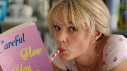 In a scene from Promising Young Woman, Cassie (Carey Mulligan) drinks from a pink straw while reading a book with a pink cover.