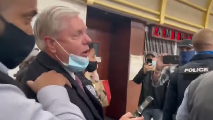 Lindsey Graham is escorted through an airport by police as people yell at him.