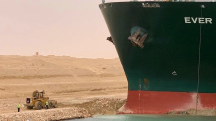 The stuck container ship Ever Given next to a tiny little digger working to get it out.