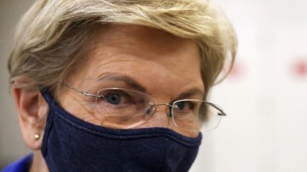 A closeup of Elizabeth Warren, wearing a mask, looking into the camera