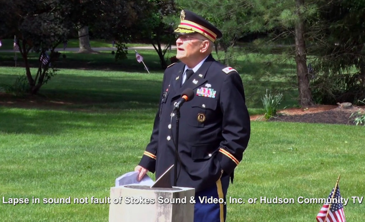 An elderly veteran in uniform speaks at a ceremony outdoors.