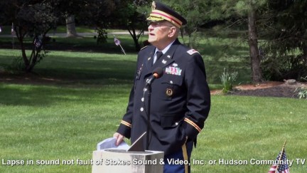 An elderly veteran in uniform speaks at a ceremony outdoors.