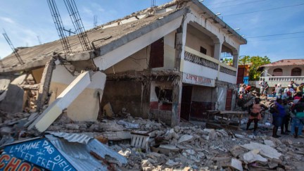 People stand by the debris of a collapsed building after a 7.2-magnitude earthquake struck Haiti on August 16, 2021