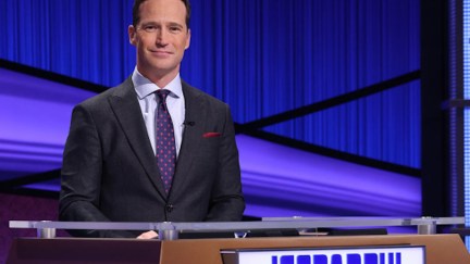 Mike Richards stands at the host podium during an episode of Jeopardy.