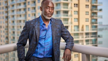 Actor Michael K. Williams in a suit and blue shirt posed on a balcony