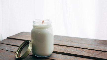 A white unlit candle sits on a wooden table.