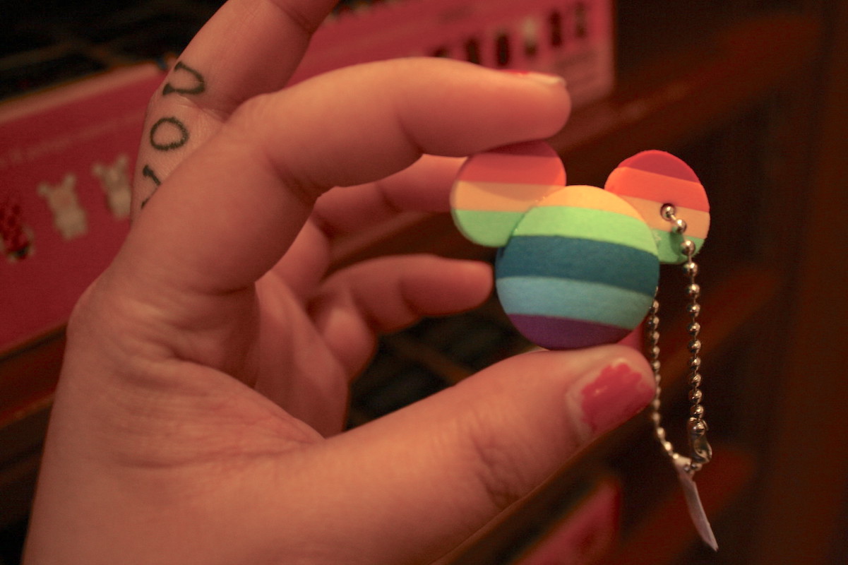 A white hand holds a keychain in the shape of mickey mouse ears in rainbow print