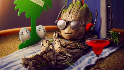 Baby Groot in sunglasses, sitting on a beach towel next to a palm tree air freshener.