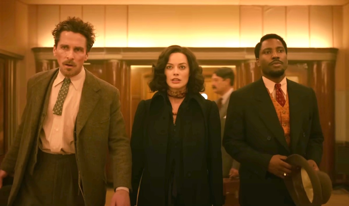 Christian Bale, Margot Robbie, John David Washington dressed in 1930s-era costumes, standing together looking haggard in a scene from Amsterdam.