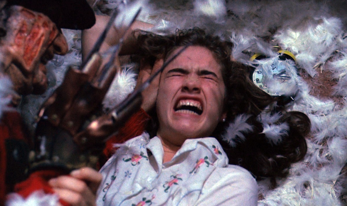 a woman makes a scared expression, as Freddy Krueger's clawed hand attempts to attack her