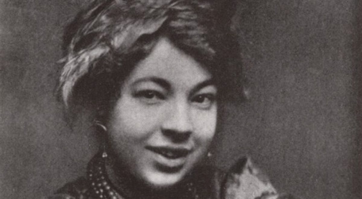 Photograph of Pamela Colman Smith, wearing a scarf in her hair and a mischievous smile.