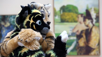 Two people in fur suits hug each other in front of a piece of artwork at the Eurofurence conference in 2015