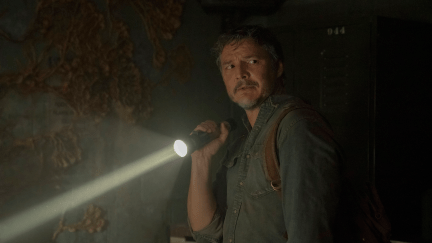 Joel Miller (Pedro Pascal) stands in a dark room, holding a flashlight in a still from 'The Last of Us'