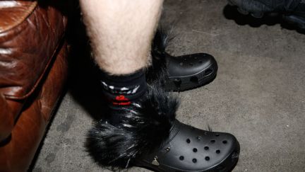 A pair of black Crocs wish black feathers on a white man's legs