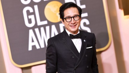 Ke Huy Quan smiles in a tuxedo with a Golden Globe Awards sign behind him.