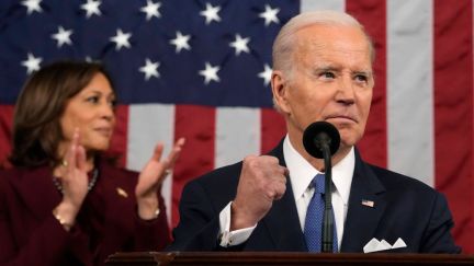 Joe Biden raises a fist while standing at a podium. Kamala Harrise claps behind him, standing in front of an American flag.