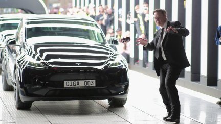 Elon Musk strikes a strange pose in front of a Tesla car.