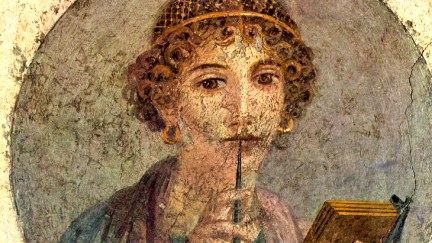 A fresco of a young ancient woman holding a stylus to her lips and a tablet in her other hand.