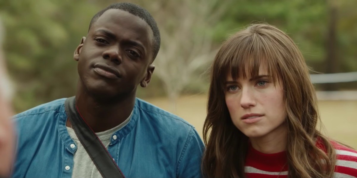 Image of Daniel Kaluuya (Chris) and Allison Williams (Rose) in 'Get Out' We see them from the shoulders up standing outdoors side by side. Chris is on the left wearing a blue jacket and a grey shirt. A camera strap hangs across his body. Rose has long, brown hair with bangs. She's wearing a red and grey striped shirt.