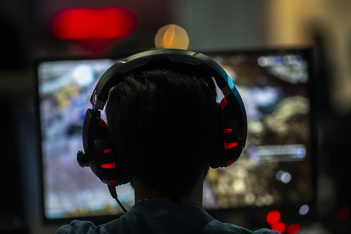 A gamer seen in silhouette from behind, wearing large headphones, looking at a screen