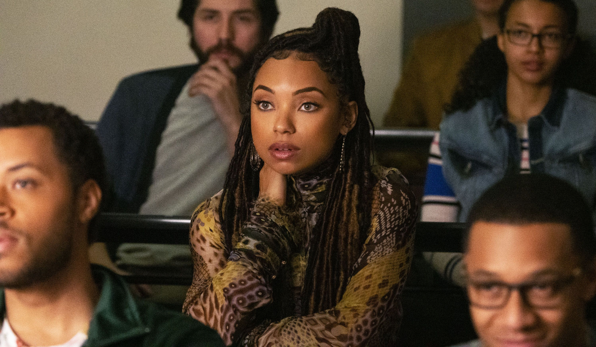 A Black woman with a worried look and braids sits in a classroom surrounded by peers