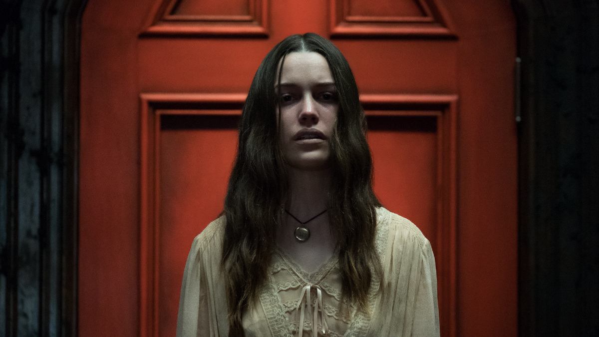 A pale woman stands in front of a creepy red door.