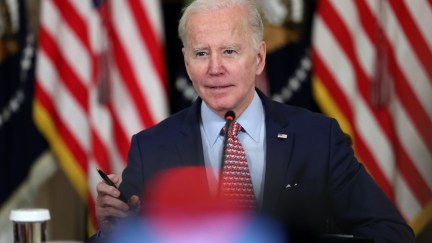 Joe Biden gives a speech from a podium in front of American flags, seen with a lens flare.