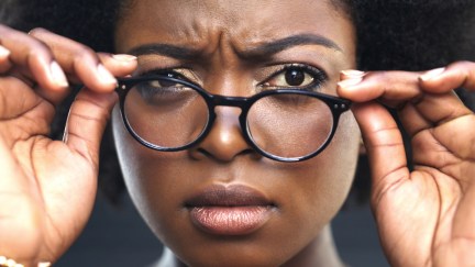 Cropped shot of a woman adjusting her glasses against a dark background