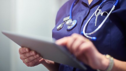 Closeup of a female doctor's torso as she looks at a digital tablet