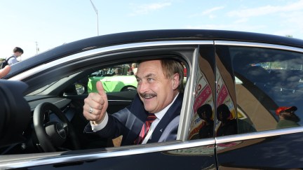 Mike Lindell gives a thumbs up while driving a car.