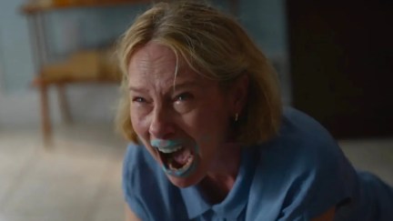 Grace screams in anger, with blue paint on her mouth, while kneeling on the floor. Still from Beau is Afraid.