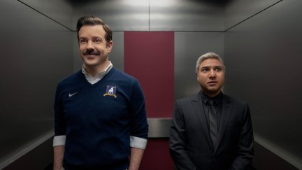 Ted and Nate stand in an elevator together. Ted is smiling, but Nate looks pensive.