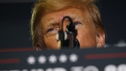 A close up of Donald Trump's angry eyes peering out from over a podium at a campaign rally.