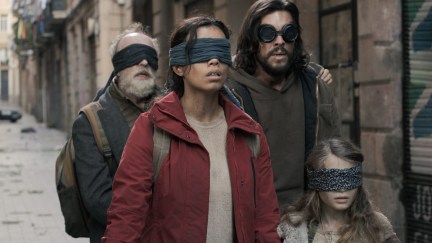 People walk down a city sidewalk with blindfolds covering their eyes in 'Bird Box Barcelona'