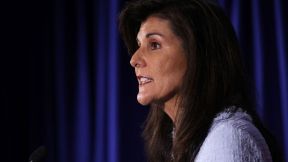 Nikki Haley speaks in front of a podium in front of a blue curtain.