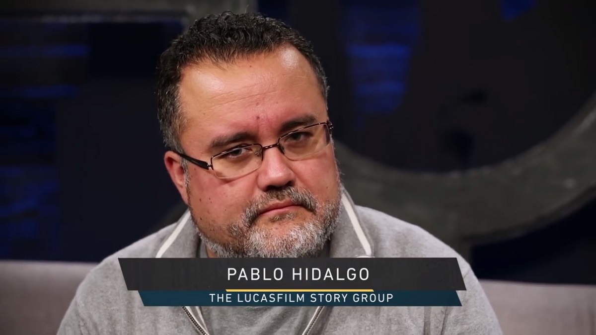 Screencap of Pablo Hidalgo on 'The Star Wars Show'. It's a close-up of Hidalgo, who is a white Chilean with dark, slicked back hair, glasses, and a salt and pepper beard. He's wearing a grey polo shirt. A chyron on the screen reads "Pablo Hidalgo: The Lucasfilm Story Group"